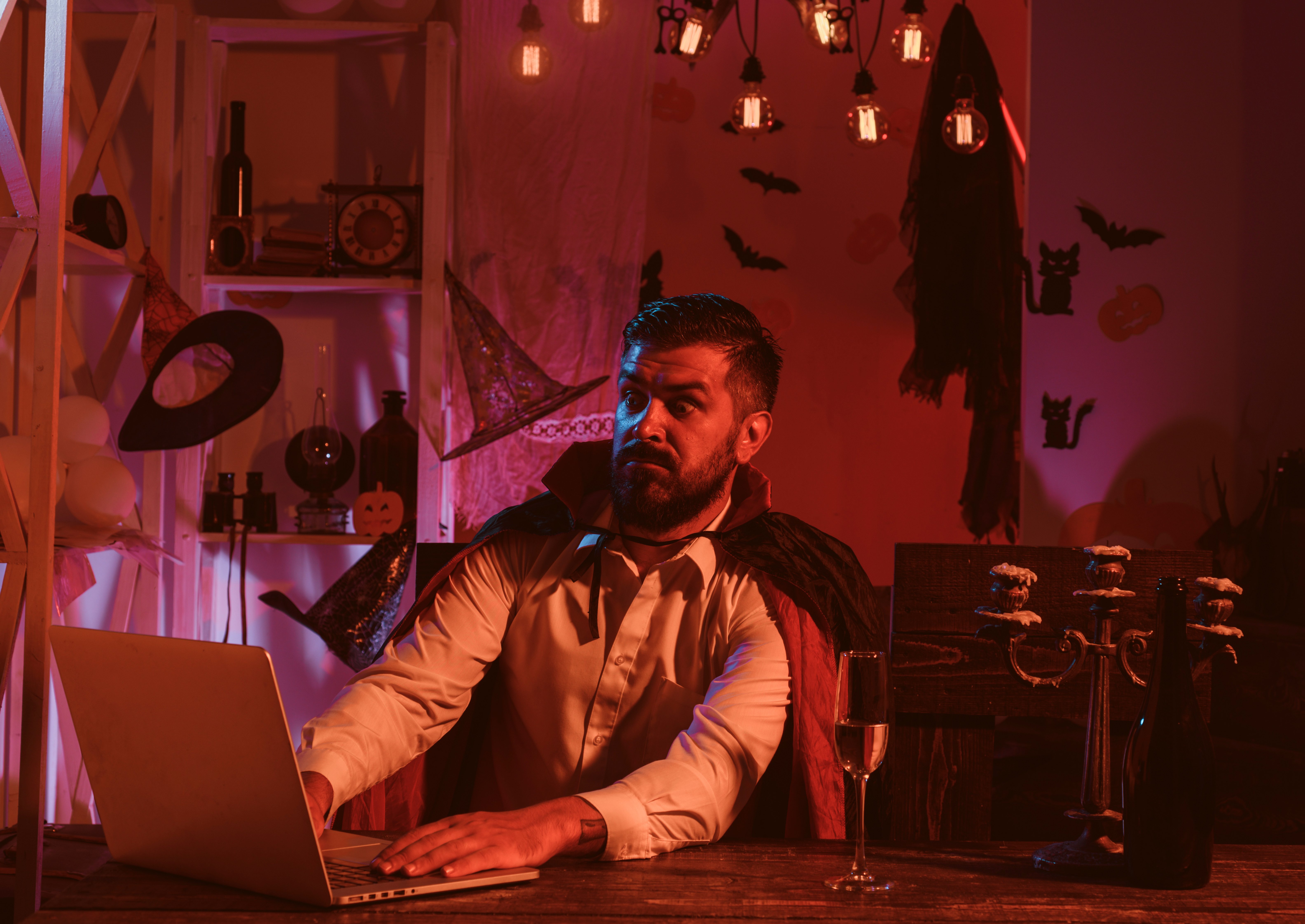 Scary movie on Halloween. A man with surprise and fear looks at the laptop monitor. Black Friday. Online shopping for Halloween. Computer wizard. Magical technology